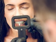 Unbekannter Zahnarzt pflückt Farbstoff eines Zahnes für Frau, die mit geschlossenen Augen sitzt — Stockfoto