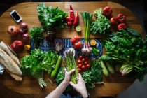 Schnittansicht weiblicher Hände, die Potherbs von einem eleganten Tisch mit frischen gesunden Gemüse- und Obstzutaten von oben holen — Stockfoto