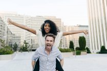 Man giving piggyback ride to African-American woman while having fun on city street together — Stock Photo