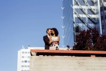 Багаторасова пара обіймається перед сучасними будівлями — стокове фото