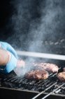 Human hands cooking raw burger patties roasting on grid of barbecue grill outdoors — Stock Photo