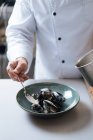 Chef garnishing Nordic seafood dish with mussels and cream sauce on plate — Stock Photo