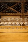Row of elegant shiny glasses standing on wooden table in wine cellar with wine bottles on shelves on background — Stock Photo