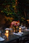 Setting table decorated with candles and flowers at night on backyard — Stock Photo