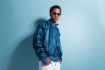 Young black man in blue outfit and sunglasses standing on blue background — Stock Photo