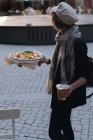 Mujer sosteniendo un vaso de cerveza y pizza mientras camina en la cafetería exterior - foto de stock