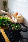 Mano umana mescolando foglie di spinaci in vaso sul fornello a gas — Foto stock