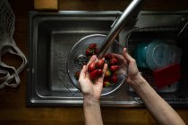 Mani umane lavare le fragole sotto rubinetto lavandino — Foto stock
