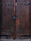 Close-up shot of old wooden door with ornamental carving and metal rivets with hanging lock — Stock Photo