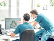Dos dentistas co-trabajando y discutiendo mientras modelan la mandíbula en la computadora en el laboratorio - foto de stock