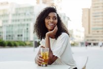 Mulher afro-americana encantadora segurando vidro de bebida no café ao ar livre — Fotografia de Stock