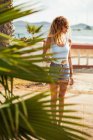 Donna in costume da bagno e pantaloncini di jeans guardando lontano sulla costa — Foto stock