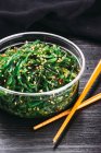 Chopsticks and bowl of yummy seaweed salad on black wooden tabletop — Stock Photo