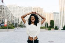 Laughing African-American woman standing on street with hands up and looking at camera — Stock Photo