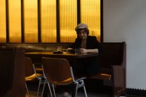Junge hübsche Frau mit Mütze sitzt allein am Tisch in einem modernen Restaurant und liest sich durch die Speisekarte — Stockfoto