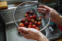 Mani umane che tengono il colino di fragole fresche sopra lavandino in cucina — Foto stock