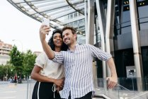 Black woman and caucasian man posing for selfie while standing on background of modern city — Stock Photo