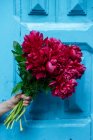 Main tenant un bouquet vif de pivoines roses devant la porte bleue en bois — Photo de stock