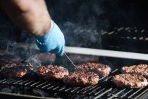 Mão humana cozinhando hambúrgueres crus assar na grade de churrasqueira ao ar livre — Fotografia de Stock