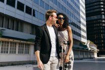 Elegantes, multiethnisches Paar, das an sonnigen Tagen gemeinsam auf der Stadtstraße spaziert — Stockfoto