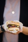 Close-up of female hand holding burger wrapped in paper — Stock Photo