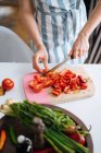 Mãos femininas cortando pimentas vermelhas e tomates em tábua de cortar — Fotografia de Stock