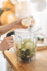 Mãos femininas colocando pêra na tigela de liquidificador para smoothie verde — Fotografia de Stock