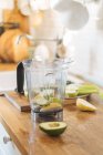 Пластиковая чашка блендера со свежим авокадо и грушей для смузи на деревянном кухонном столе — стоковое фото