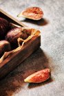 Fresh figs in wooden box with slices on grey surface — Stock Photo