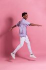 Lächelnder junger schwarzer Mann in weißer Jeans und Hemd springt vor rosa Hintergrund — Stockfoto