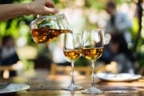 Mano umana versando vino bianco da brocca di vetro in bicchieri sul tavolo all'aperto — Foto stock