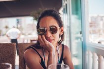 Young woman in sunglasses sitting in cafe in summer — Stock Photo
