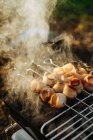 Close-up de grelha portátil com carvão em chamas e espetos com tiras de bacon grelhar — Fotografia de Stock