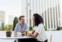Sorrindo casal multirracial olhando uns para os outros enquanto passavam tempo no café ao ar livre juntos — Fotografia de Stock
