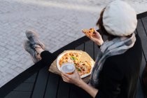 Жінка сидить на подіумі на вулиці зі склянкою пива і виймає піцу — стокове фото