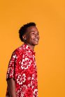 Giovane uomo afro-americano sorridente che indossa una camicia da spiaggia colorata e distoglie lo sguardo sullo sfondo arancione — Foto stock