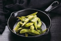 Heap de feijão verde não descascado na frigideira na mesa de madeira preta — Fotografia de Stock