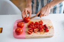 Mains féminines coupant poivrons rouges et tomates sur planche à découper — Photo de stock