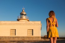 Жінка в одязі стоїть на береговій лінії перед маяком — стокове фото