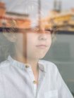 Sad little boy looking through glass — Stock Photo