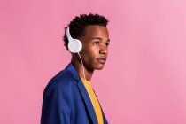 Thoughtful stylish man in jacket and headphones on pink background — Stock Photo
