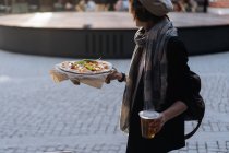 Femme tenant un verre de bière et de pizza tout en marchant dans la cafétéria extérieure — Photo de stock
