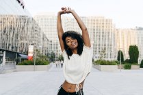 Смеющаяся афроамериканка, стоящая на улице с поднятыми руками и смотрящая в камеру — стоковое фото