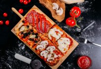 Pizza cortada con queso, salsa y berenjenas en rodajas sobre tabla de madera sobre mesa oscura - foto de stock