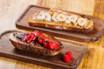 Toasts garnished with banana, strawberry and different toppings on wooden boards — Stock Photo