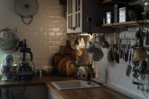 Interior da cozinha com paredes de azulejos brancos e abundância de utensílios e aparelhos compostos em prateleiras e bancada — Fotografia de Stock