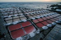 Picturesque view of small rectangular crystallization ponds with ocean water and produced salt in piles around on rocky sea coast at sunset in Spain — Stock Photo