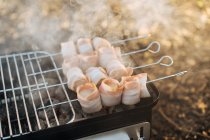 Крупный план переносной сковородки с горящим углем и шампуры с беконом гриля полосы — стоковое фото