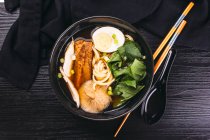 Bowl of delicious ramen on black wooden tabletop with chopsticks and ceramic spoon — Stock Photo