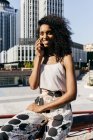 Елегантний афро-американських жінка, посміхаючись і говорити на смартфоні сидячи на паркан на місто вулиці — стокове фото